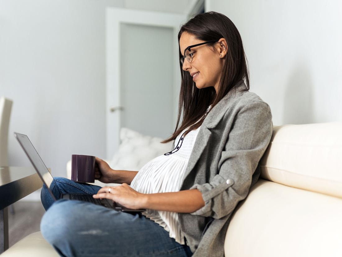 Pregnant Woman Sitting On Couch At Home While Using The Laptop